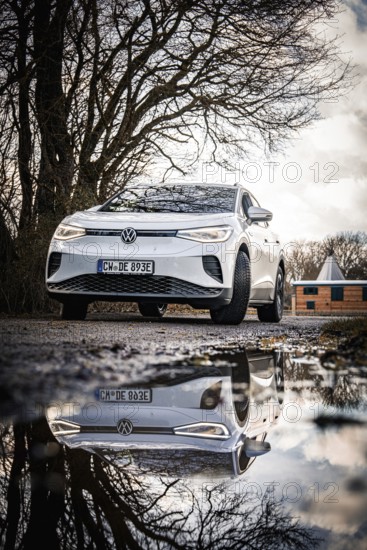A white car with a reflected image is standing on a road in front of winter trees, VW ID4 electric car, Deer Carsharing, Calw, Germany