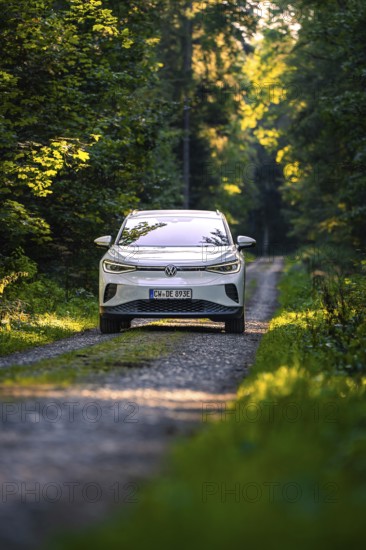 A white car drives on a forest path, lined with trees, at dawn, VW ID4 electric car, deer car sharing, Calw, Germany