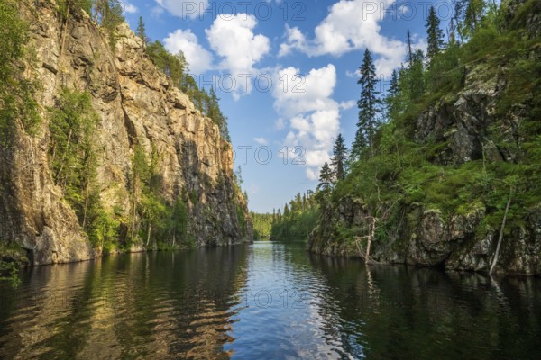 A calm lake lies in a wooded gorge, surrounded by tall rocks and reflecting the sky covered with clouds Julma-Ölkky Canyon Gorge, Hossa National Park, Irni, Northern Ostrobothnia, Finland