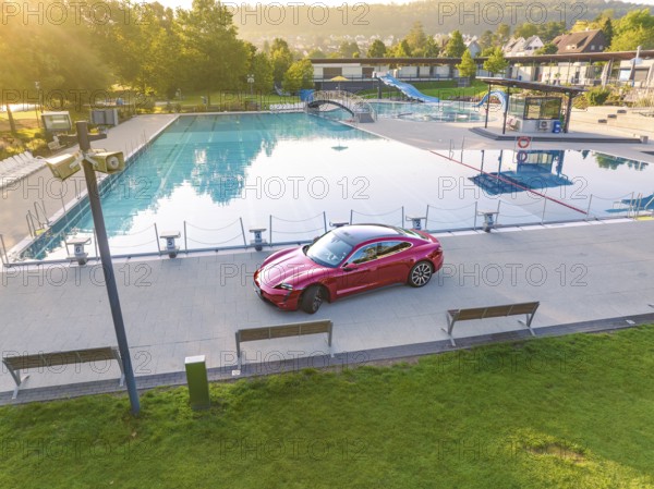 Red sports car at the edge of a swimming pool in a park during daylight, Porsche Taycan, Deer Carsharing, Calw, Germany