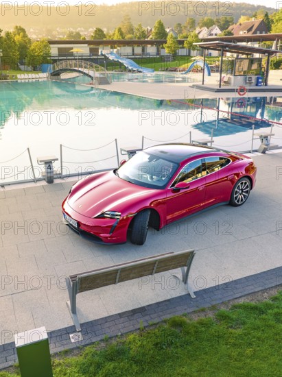 Red sports car parked next to a swimming pool and park bench in daylight, Porsche Taycan, Deer Carsharing, Calw, Germany