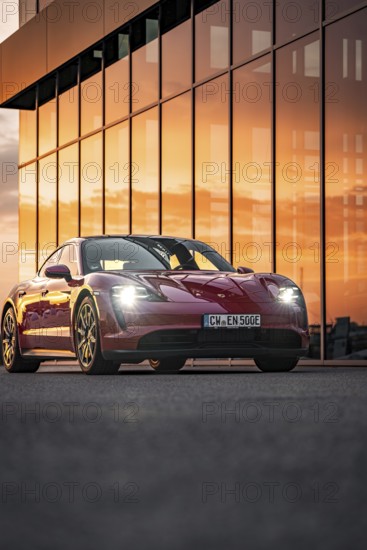Red sports car reflected in the glass façade of a building at sunset, Porsche Taycan, Deer Carsharing, Calw, Germany