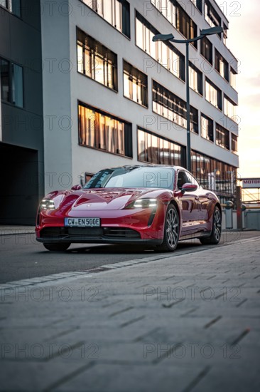 Red sports car parked in front of a modern building in the city at dusk, Porsche Taycan, Deer Carsharing, Calw, Germany