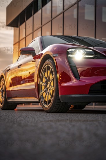 Red sports car reflected in front of a glass façade at sunset, Porsche Taycan, Deer Carsharing, Calw, Germany