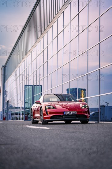 Red car standing in front of a modern glass building, reflecting sky in the background, Porsche Taycan, Deer Carsharing, Calw, Germany