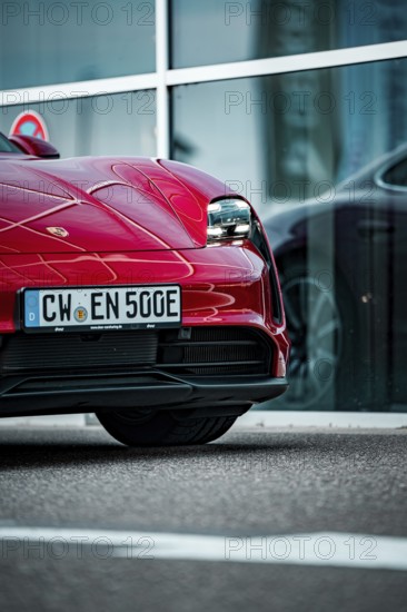Partial view of the front of a modern red sports car in front of a glass façade, Porsche Taycan, Deer Carsharing, Calw, Germany