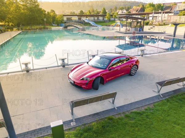 Red Porsche Taycan in parking lot next to swimming pool in relaxed landscape, Porsche Taycan, Deer Carsharing, Calw, Germany