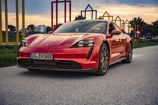 Red sports car on a road in front of a colorful art installation at sunset, Porsche Taycan, Deer Carsharing, Calw, Germany