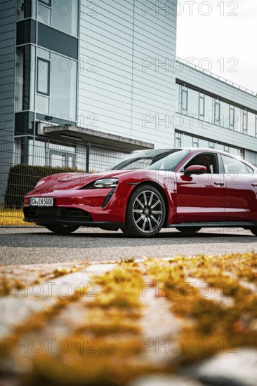 Modern red sports car in front of an office building on the street in daylight, Porsche Taycan, Deer Carsharing, Calw, Germany