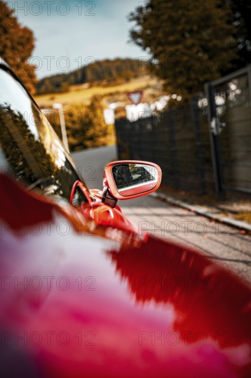 Side mirror of a red car with reflections of a landscape, autumn environment, Porsche Taycan, Deer Carsharing, Calw, Germany