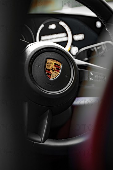 Close-up of a steering wheel with a distinctive logo in the background, Porsche Taycan, Deer Carsharing, Calw, Germany