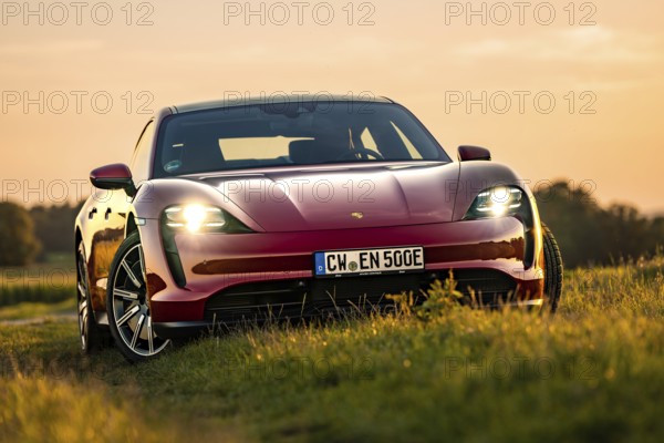 Red car in a meadow at dusk, natural environment, Porsche Taycan, Deer Carsharing, Calw, Germany