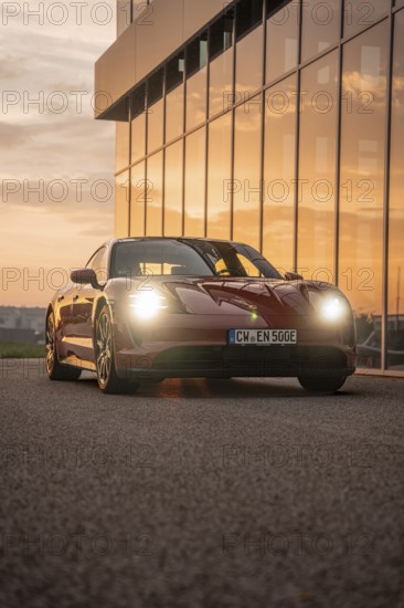 Red car at sunset near a modern building with reflections, Porsche Taycan, Deer Carsharing, Calw, Germany