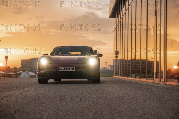 Red car in an urban setting at sunset, reflective windows, Porsche Taycan, Deer Carsharing, Calw, Germany