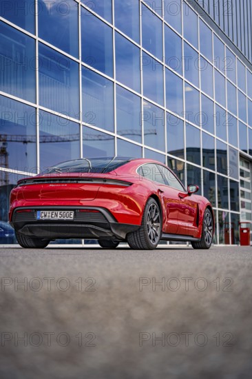 Modern red car in front of a building with glass façade, urban atmosphere, Porsche Taycan, Deer Carsharing, Calw, Germany