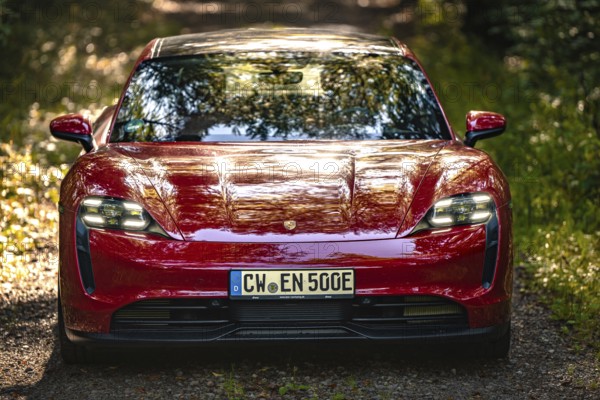Close-up of a red car on a forest path, sunbeams in nature, Porsche Taycan, deer car sharing, Calw, Germany