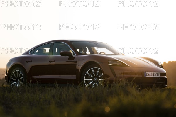 Red car in a meadow, sunset in the background, elegant lines, Porsche Taycan, Deer Carsharing, Calw, Germany