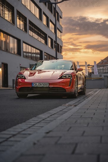 A red sports car in front of city buildings in the evening mood, Porsche Taycan, Deer Carsharing. Calw, Germany