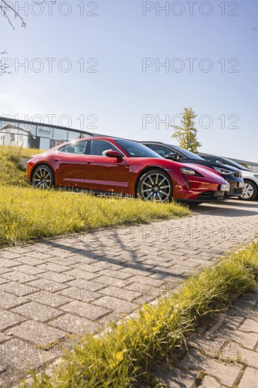 A red sports car is parked on a paved path in sunshine, Porsche Taycan, deer car sharing. Calw, Germany