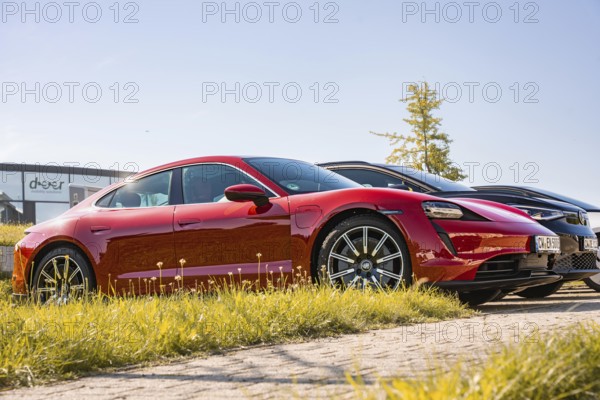 When the sun is shining, a red sports car parks outside next to other vehicles, Porsche Taycan, Deer Carsharing. Calw, Germany