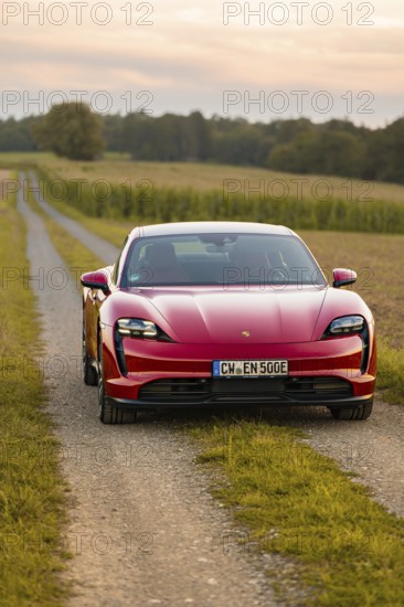 A red sports car on a gravel road through a rural area at sunset, Porsche Taycan, deer car sharing. Calw, Germany