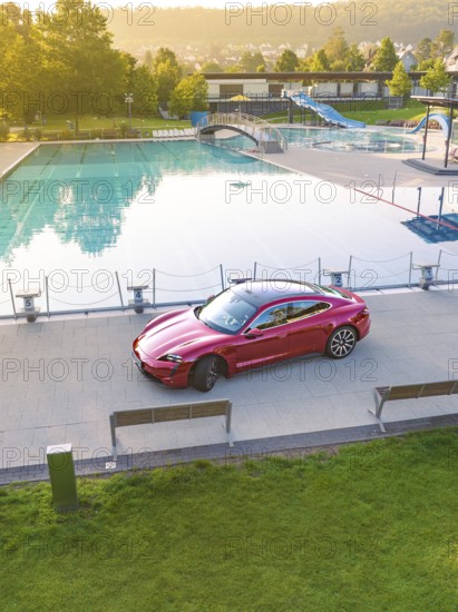 Red car parked next to swimming pool in urban area, Porsche Taycan, deer car sharing. Calw, Germany