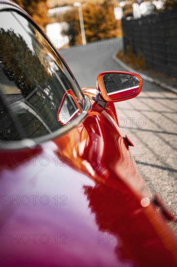 Red car with side mirror on a road with reflections, Porsche Taycan, Deer car sharing. Calw, Germany