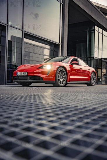 Red sports car in front of a modern glass building at dusk, Porsche Taycan, deer car sharing. Calw, Germany