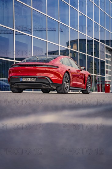 Red car in front of a glass façade with an urban background, Porsche Taycan, Deer car sharing. Calw, Germany