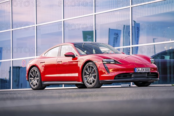 Red sports car in front of a modern glass façade at dusk, Porsche Taycan, deer car sharing. Calw, Germany