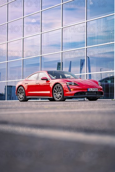 Red sports car in front of a modern building in the evening light, Porsche Taycan, Deer Carsharing. Calw, Germany