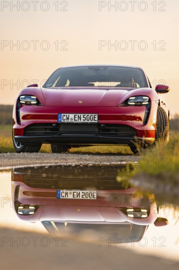 Red car reflected in water on the road at sunrise, Porsche Taycan, Deer car sharing. Calw, Germany