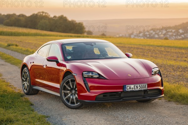 A red sports car drives on an asphalt road through rural landscape, Porsche Taycan, deer car sharing. Calw, Germany