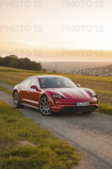 A red sports car on a rural road at sunset next to fields, Porsche Taycan, deer car sharing. Calw, Germany