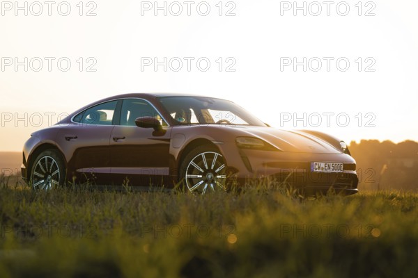 Red car parked at sunset in a field with golden light, Porsche Taycan, deer car sharing. Calw, Germany