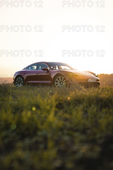 Red car positioned on a field at golden sunset, Porsche Taycan, Deer car sharing. Calw, Germany