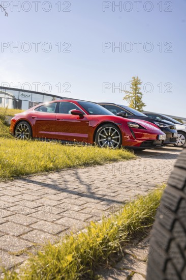 A red sports car in a parking lot in the sun viewed from a low perspective, Porsche Taycan, Deer Carsharing. Calw, Germany
