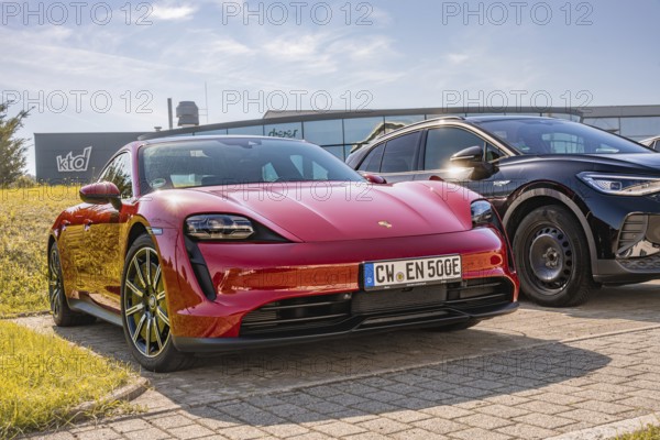 A red sports car in a parking lot in sunshine next to a black car, Porsche Taycan, deer car sharing. Calw, Germany
