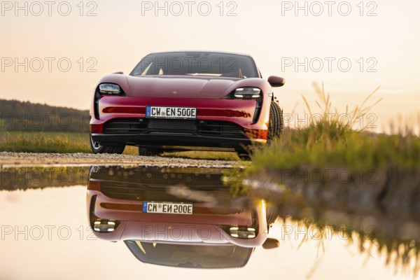 Red car reflected in a body of water at sunrise, Porsche Taycan, deer car sharing. Calw, Germany