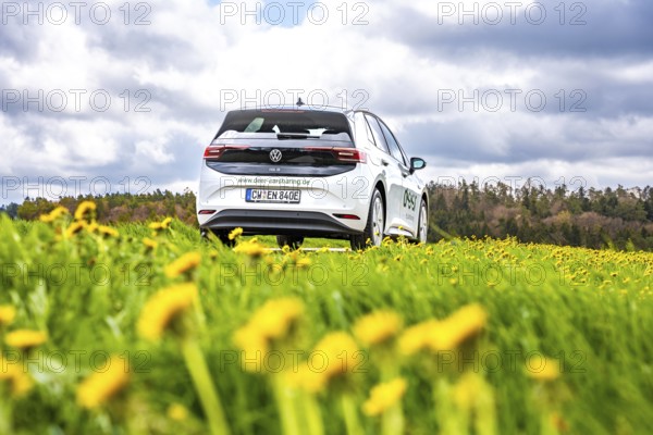 A white car is parked on a flower meadow under a cloudy sky, ID3 VW, deer car sharing. Calw, Germany