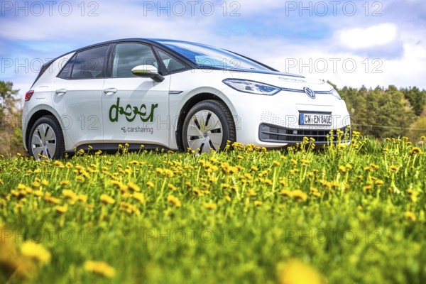 A white car sharing car on a blooming meadow under bright skies, ID3 VW, deer car sharing. Calw, Germany
