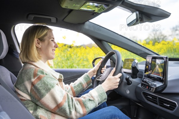 A smiling woman sits in a car and drives through a blooming landscape, ID3 VW, deer car sharing. Calw, Germany