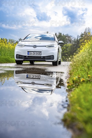 White car on country road, reflected in puddle, surrounded by nature under cloudy sky, ID3 VW, deer car sharing. Calw, Germany