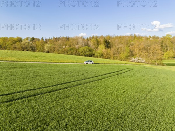 Car on country road surrounded by green fields under clear sky, ID3 VW, deer car sharing. Calw, Germany