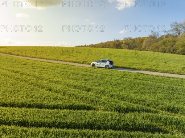 Car on a narrow country road through wide green fields under a sunny sky, ID3 VW, deer car sharing. Calw, Germany