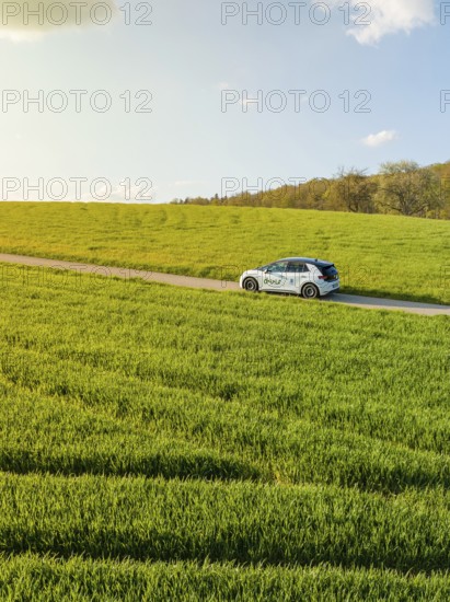 Car on a road between green fields, row of trees in the background, ID3 VW, deer car sharing. Calw, Germany