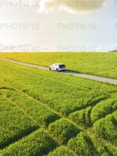 Car driving on a country road through vast green fields in sunlight, ID3 VW, deer car sharing. Calw, Germany
