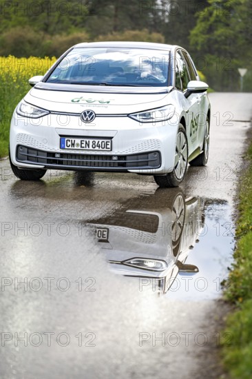 Car on wet road with clear reflection in the puddle, surrounded by green nature, ID3 VW, deer car sharing. Calw, Germany