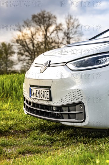 Close-up of a car nose with raindrops on green field in front of trees, ID3 VW, deer car sharing. Calw, Germany