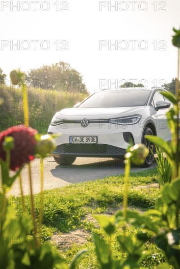 A white car is parked in a meadow surrounded by flowers in sunlight, VW ID4 electric car, Deer Carsharing, Calw, Germany